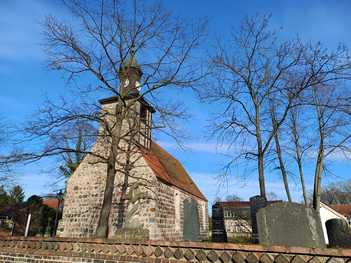 Brandenburgische Feldsteinkirche mit historischem Friedhof in ruhiger ländlicher Umgebung. Die Szene strahlt Geschichte, Stille und Würde aus – ein Ort des Gedenkens und Glaubens.
