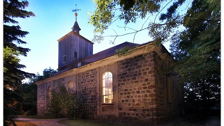 Kleine, charmante evangelische Dorfkirche, die durch ihre Beleuchtung und den Kontrast zwischen warmem Innenlicht und kühlem Außenlicht besonders feierlich wirkt.