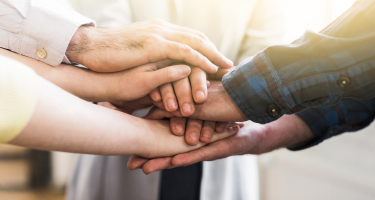 Drei paar Hände die abwechselnd aufeinenander liegen.
