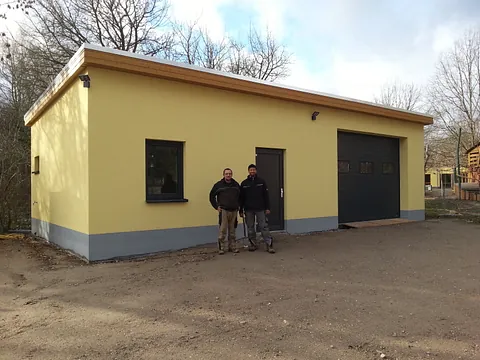 Gelbes Haus mit den Hausmeistern davor, das Haus dient als Werkstatt.